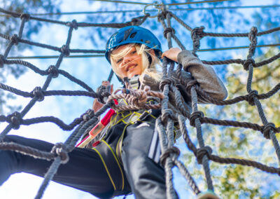 Happy girl climbing through a rope hurdle in Skypark Vaxholm.